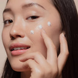 Woman applying Korean skincare essence to glowing cheek, close-up of healthy skin
