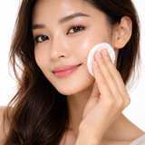 Woman applying a white cream pad to her face against a white background